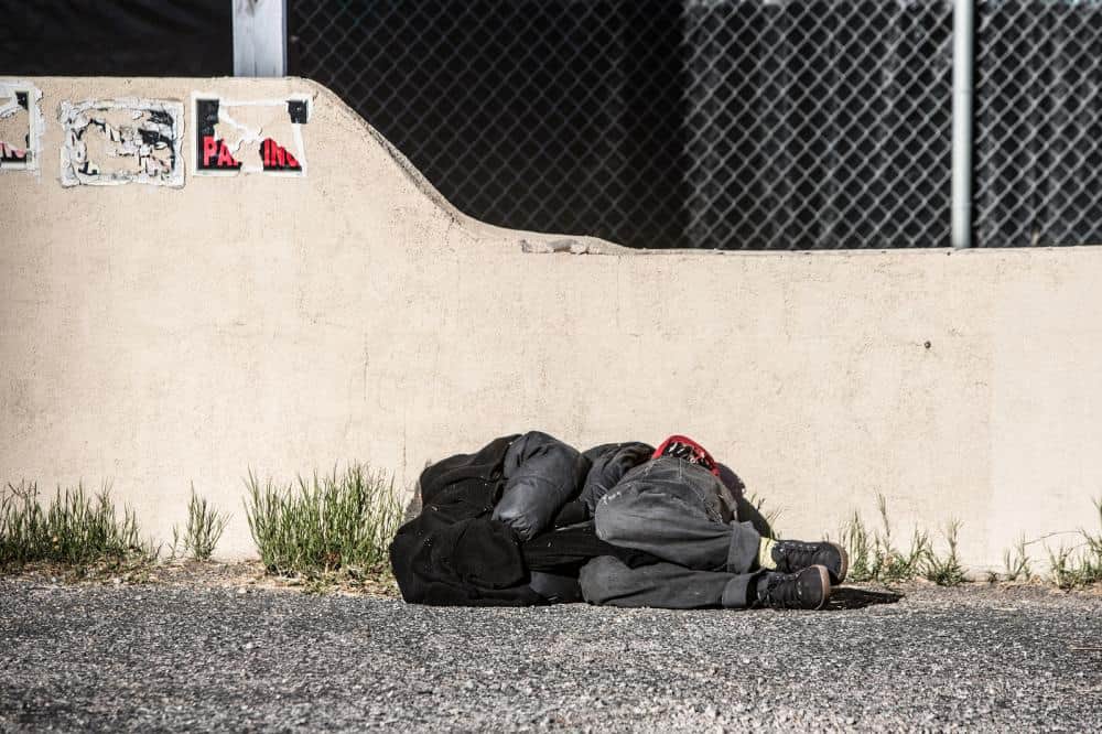 photo of a man covering his head and sleeping in a parking lot